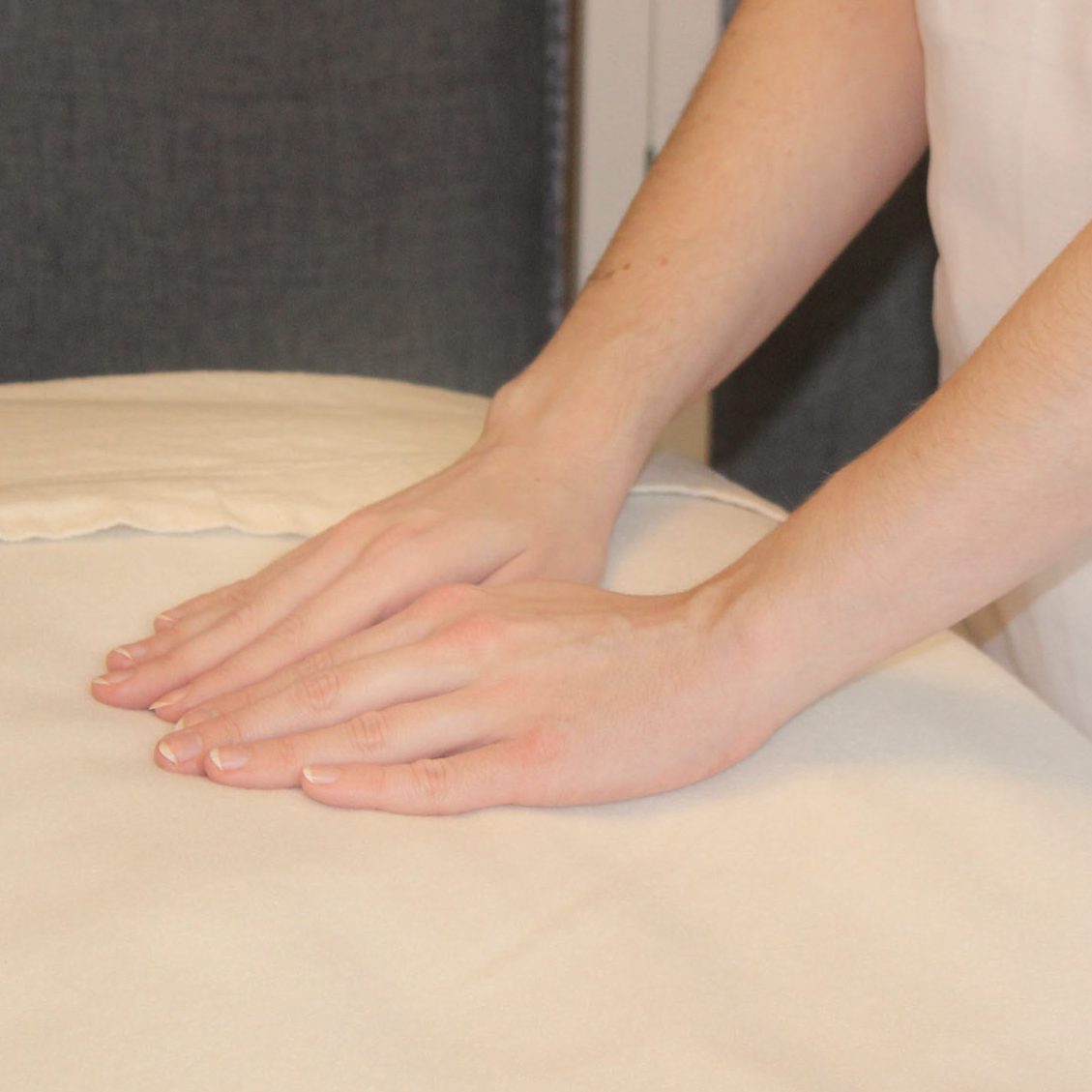 Die Reiki-Meistern hat ihre Hände dicht aneinander auf eine weiße Decke gelegt. Durch das Handauflegen kann sie Reiki übertragen.