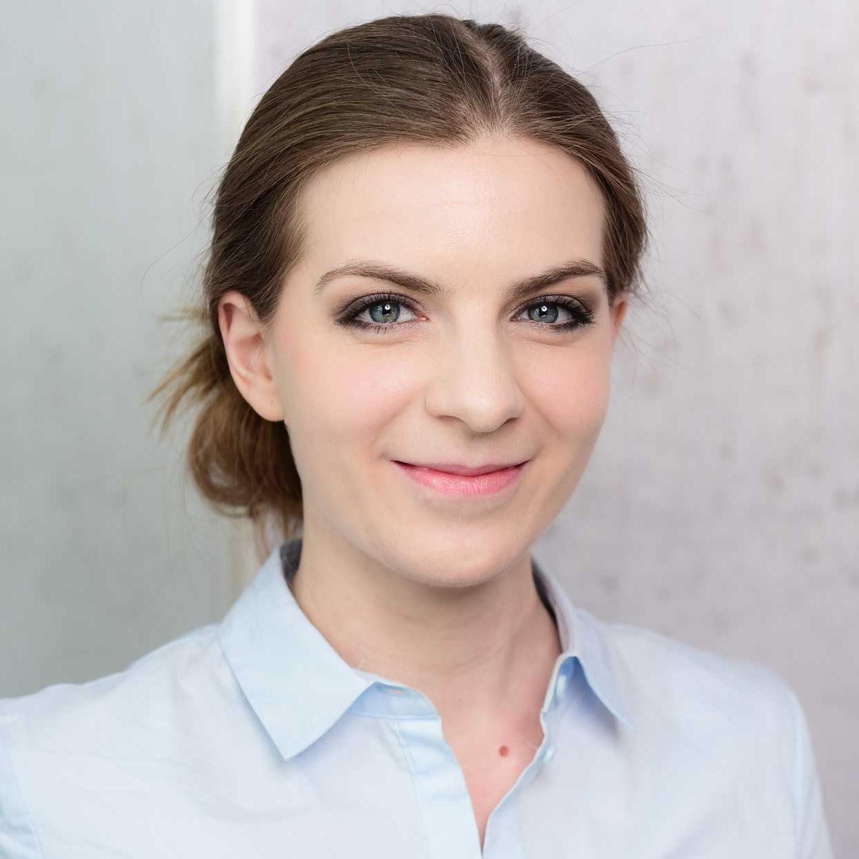  Julia Escher: Sie ist eine blonde Frau mit blauen Augen. Ihr Haar ist zusammengenkotet. Sie trägt ein blaues Hend und lächelt freundlich.