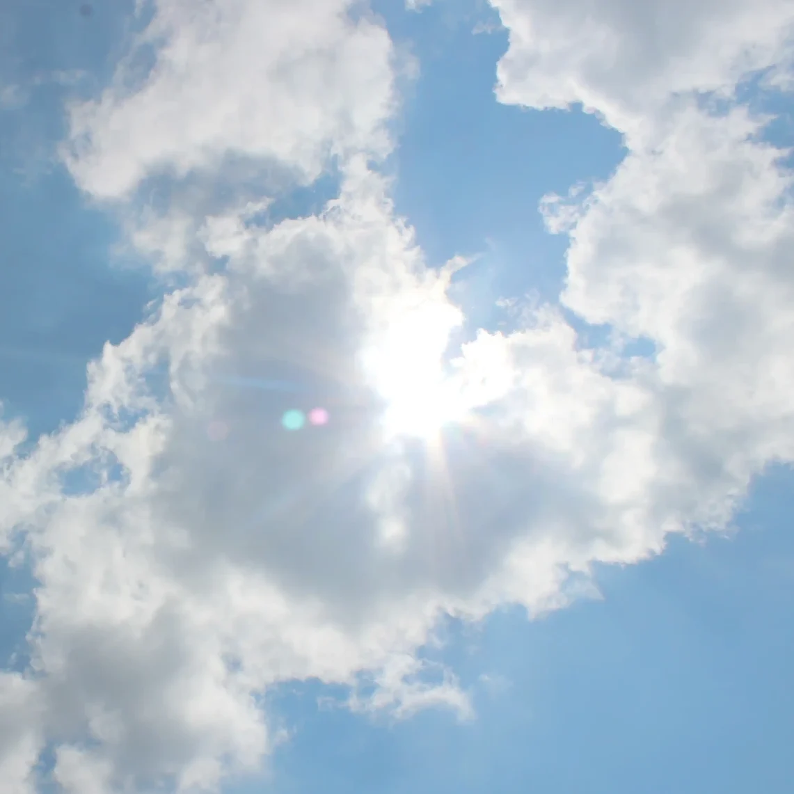 Ein blauer Himmel mit weißen Wolken, durch die die Sonne herzförmig scheint
