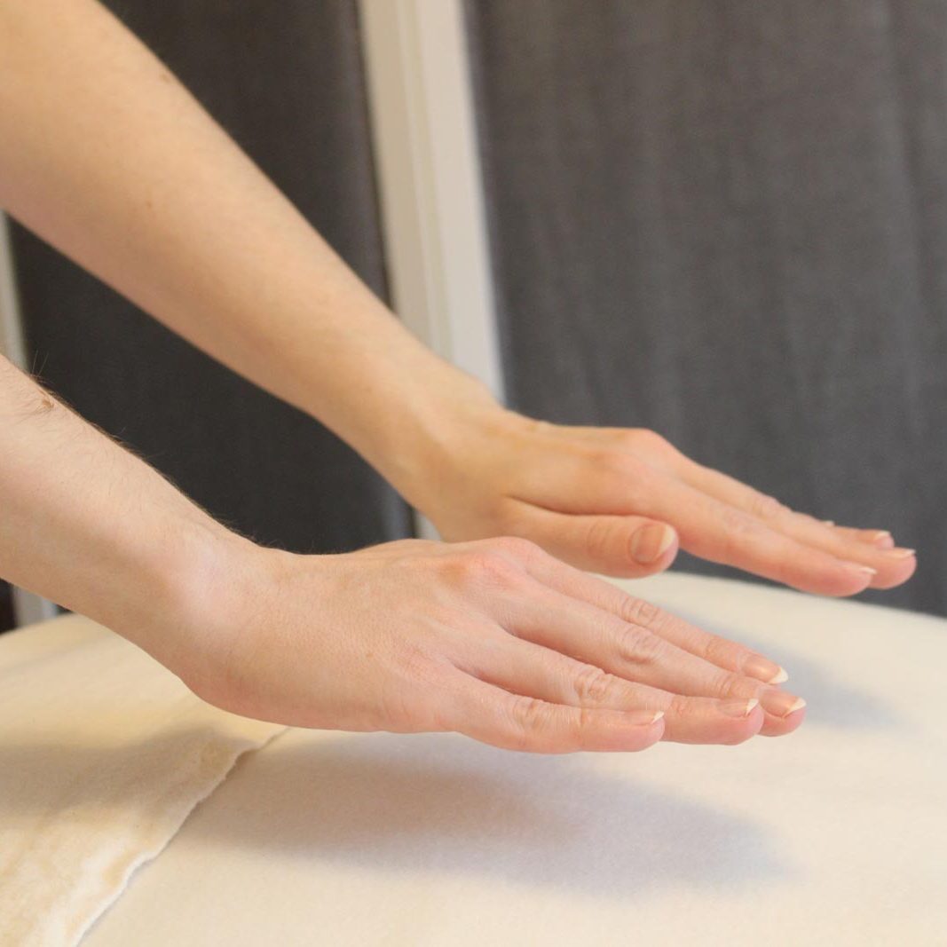 Die Hände der Reiki-Meisterin sind zu sehen, wie sie sie über eine weiße Decke hält und dabei Reiki überträgt.